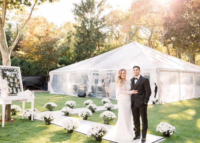 a bride and groom taking a photo with a wedding tent behind them